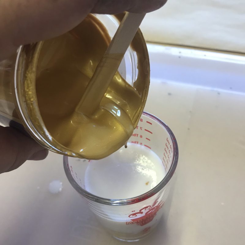 pouring gold acrylic paint into a measuring cup