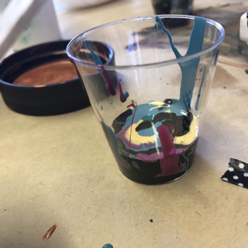 Acrylic paint layered in a clear cup black blue gold magenta ready for pouring