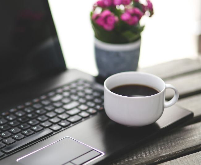 laptop on desk with cup of coffe and some flowers